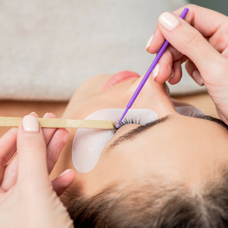 Een professionele hand die een microbrush gebruikt tijdens een wimperextension behandeling in de salon.
